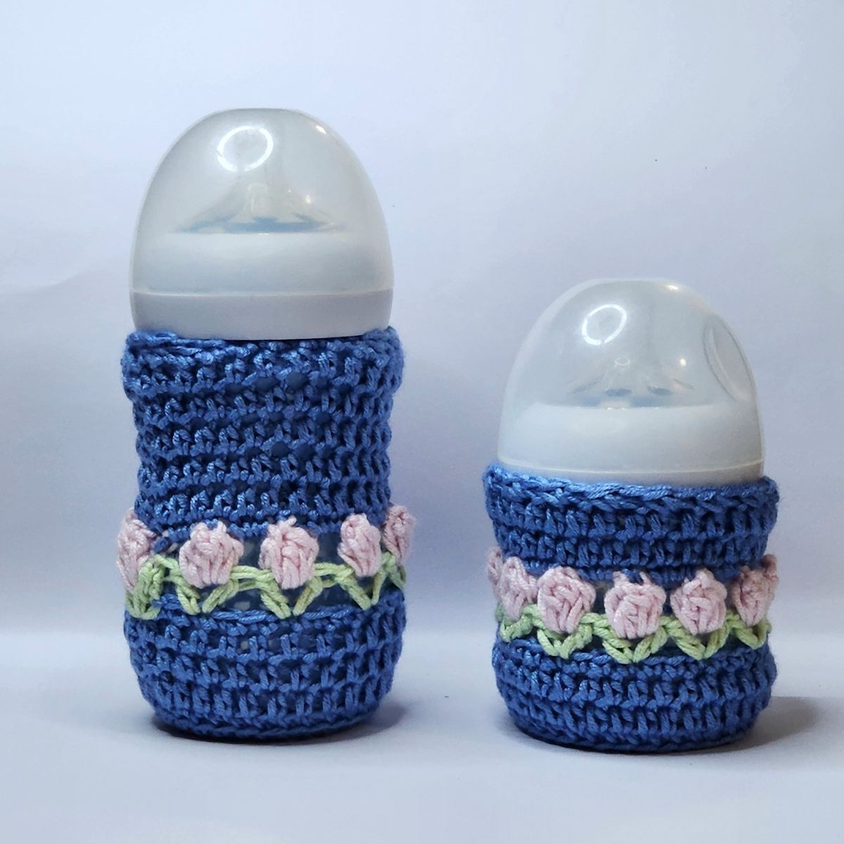 Handmade crochet baby feeder cover in blue and pink with a bow