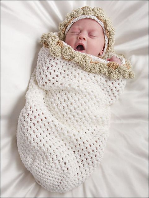 Newborn baby wrapped in a handmade crochet white cocoon with a beige hat