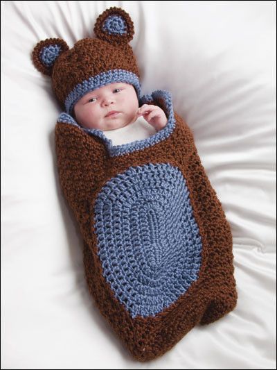 Newborn baby in a handmade crochet bear cocoon and hat set in brown and blue