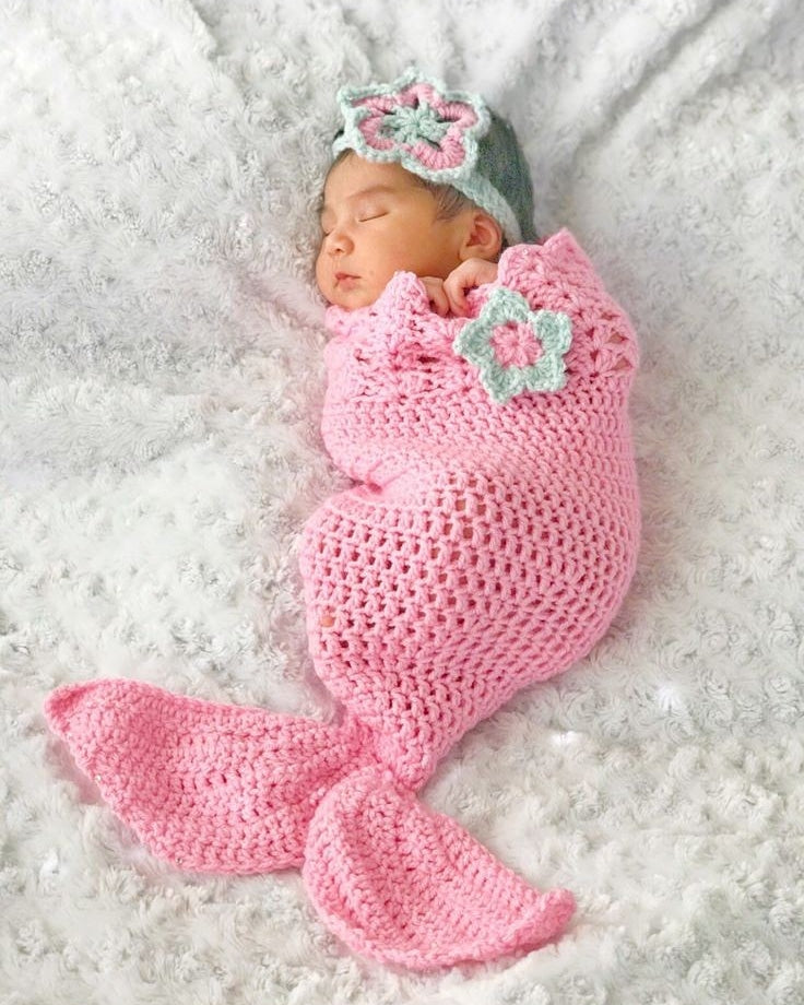 Newborn baby girl in a handmade crochet pink mermaid tail cocoon with a mint floral hat