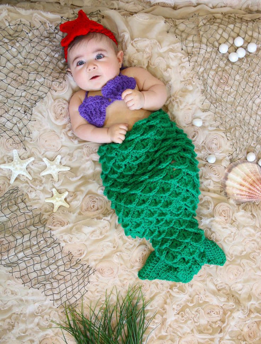 Baby girl in a handmade crochet mermaid tail cocoon set in green and purple with a red headband