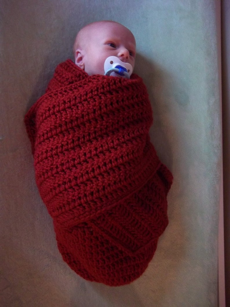 Handmade crochet baby swaddle cocoon in deep red wrapped around a newborn