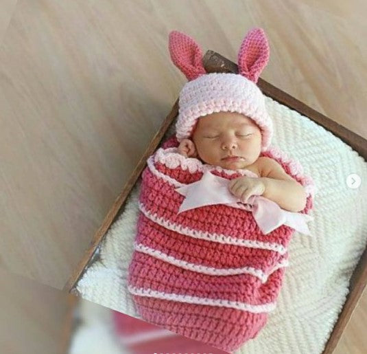 Newborn baby wrapped in a handmade crochet pink cocoon with a bunny ear hat